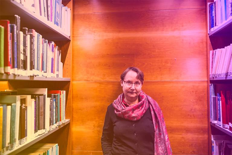 Tuula Juvonen kirjahyllyn vieressä, sateeenkaaren sävyjä.