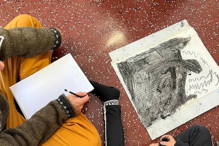 Kaksi henkilöä istuu lattialla piirroksen äärellä.