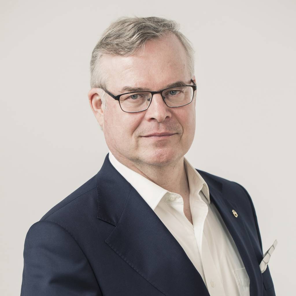 Lasse Lehtonen, jolla on harmaat hiukset ja mustapokaiset silmälasit, katsoo kameraan. Hän on pukeutunut valkoiseen kauluspaitaan ja mustaan pikkutakkiin.