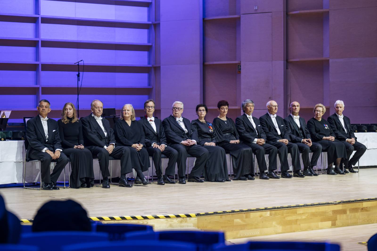 13 honorary doctors' sitting on the stage with purple light in the background.