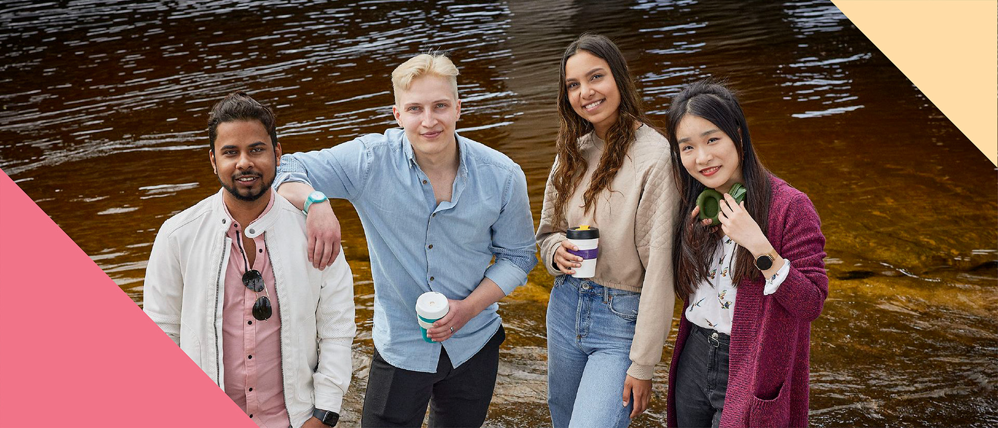 Neljä hymyilevää opiskelijaa seisoo vierekkäin järven rannalla.