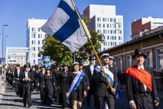 A procession on a street in Tampere, Finnish flag in front